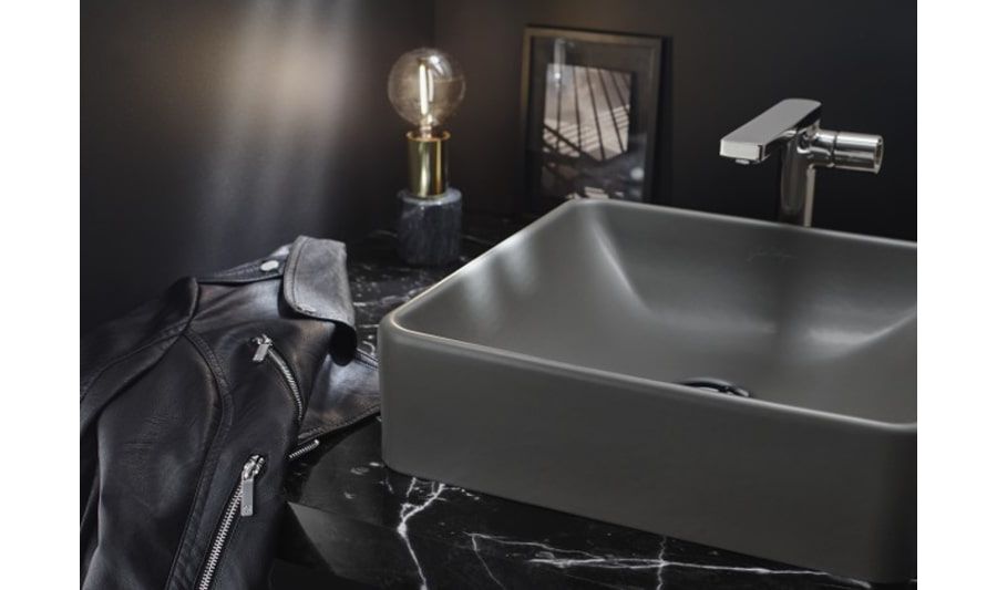 Une vasque à poser gris orage sur un plan de toilette en marbre noir veiné de blanc et une veste en cuir posée dessus