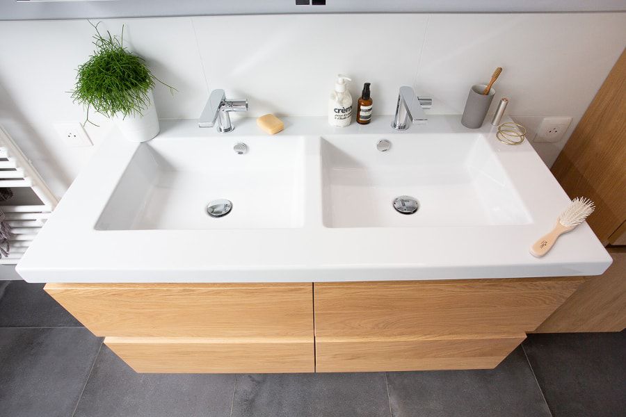 Une double vasque blanche avec un meuble sous plan-vasque en bois clair dans une salle de bains
