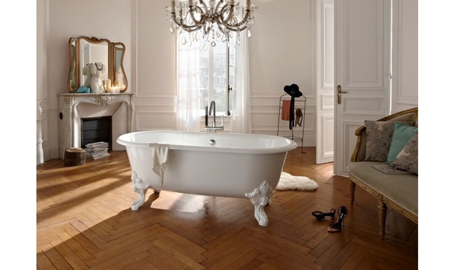 Une salle de bains parisienne au style haussmannien avec une grande baignoire d'époque blanche au milieu de la pièce, du parquet au sol, et un lustre à pampilles au plafond