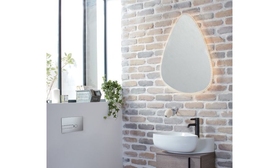 Un miroir asymétrique aux contours LED dorés dans une salle de bains décorée d'objets de décoration