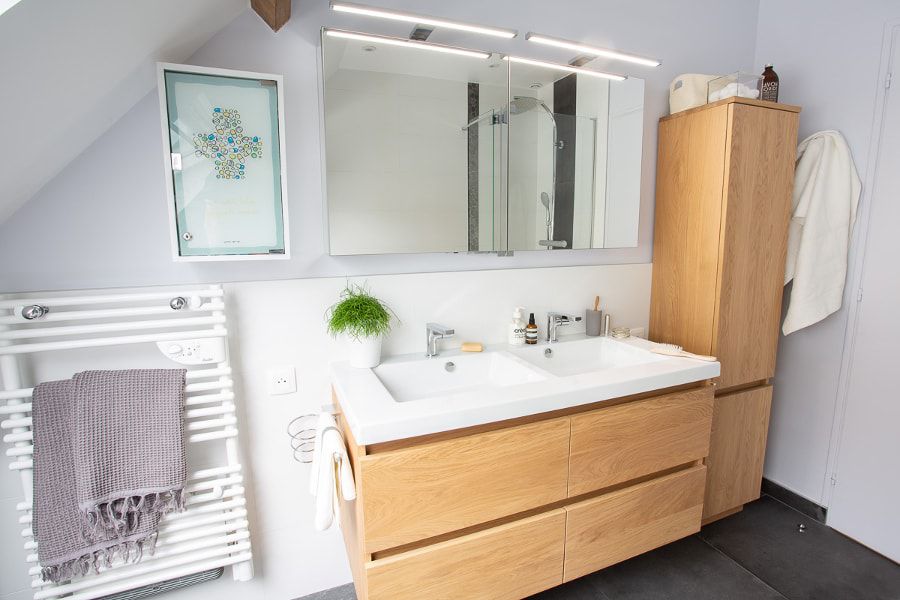 Une salle de bains aux couleurs anthracites, blanches et contenant un meuble vasque en bois clair avec des plantes vertes pour la décoration